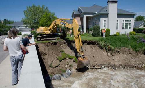 With her yard slowly slipping into Little Cottonwood Creek Penny Sim, left, watches as Sandy  City crews start securing the bank with boulders as runoff water from Little Cottonwood Creek cuts into the river banks threatening homes in the area of 8900 South 3100 East in Sandy on Monday, June 7, 2010. Steve Griffin  |  The Salt Lake Tribune