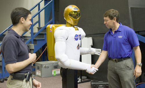 In this Aug. 4, 2010 picture provided by NASA, NASA astronaut Michael Barratt, STS-133 mission specialist, shakes hands with Robonaut 2 during a news conference in the Space Vehicle Mock-up Facility at NASA's Johnson Space Center in Houston. Ron Diftler, NASA Robonaut project manager, is at left. Robonaut 2 is hitching a one-way ride to the International Space Station on the final flight of the space shuttle Discovery scheduled for Wednesday, Nov. 3, 2010. NASA hopes one day the will assist flesh-and-bone astronauts in orbit. (AP Photo/NASA, Lauren Harnett)