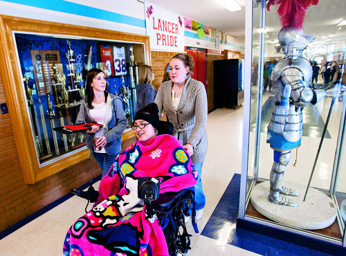 Al Hartmann  |  The Salt Lake Tribune 
Lina Nguyen was paralyzed in a car accident shortly before her junior year of high school. After a year and a half she's now returning to school at Granger High School to finish her senior year and graduate with her class.
Lina rolls to her first class and goes past the Granger High School Lancer and athletics trophy case.  Her first day back both her aides Cassandra Scott, left,  and Jennie Figueroa accompanied her to learn the routines.  Normally she will have one aide throughout the day.