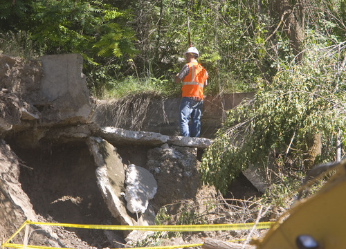 A member of a survey team on Wednesday walks across the destroyed section of concrete of the canal above Canyon Road in Logan where three people were buried in a landslide Saturday.  Earth moving equipment below worked Wednesday to stabilize the slope where the slide occured.   Al Hartmann/The Salt Lake Tribune   7/15/09