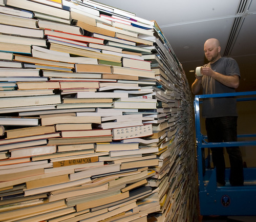 Al Hartmann   |  The Salt Lake Tribune 
Adam Bateman works from a mechanical lift touching an art piece of thousands of interlocking books that look like geological rock strata. The piece is part of the BYU Museum of Art show 