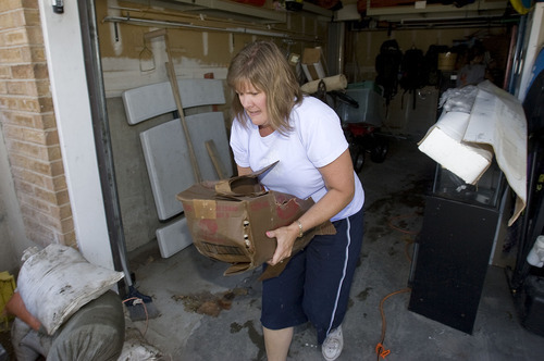Al Hartmann  |  Tribune file photo
Ruth Palmer moved a soaked box from her friend Cheryl Leithead's flooded garage after a July 26 cloudburst overwhelmed a broken storm drain. The Leitheads are among three dozen residents who have filed claims against the county, which has agreed to pay for roughly half of the damage.
