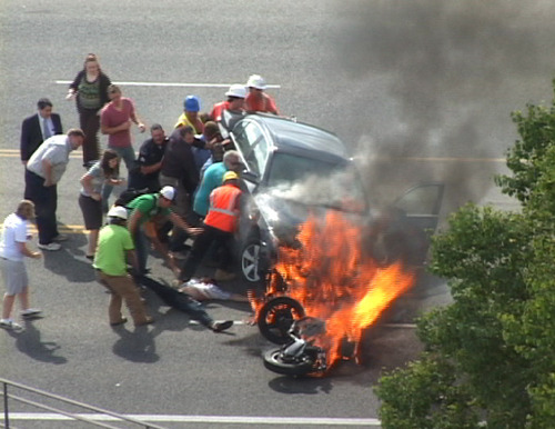 In this Monday, Sept. 12, 2011 image taken from video, a group of people tilt a burning BMW up to free Brandon Wright, on his back on the ground, who was pinned underneath after he collided with the car while riding his motorcycle on U.S. 89 in Logan, Utah.  Authorities said Wright was riding his motorcycle near the Utah State University campus in Logan when the 21-year-old collided with the BMW that was pulling out of a parking lot. Tire and skid marks on the highway indicate that Wright laid the bike down and slid along the road before colliding with the car, Assistant Police Chief Jeff Curtis said. (AP Photo/Chris Garff)