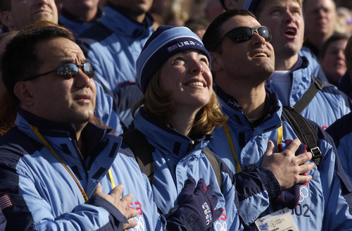 Leah Hogsten | Tribune file photo
Biathlete Andrea Nahrgang, center, coach William Tavares, left, and doctor Ed Merrens listen to the playing of the national anthem as members of the U.S. Olympic Team are greeted at the Olympic Village.