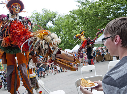 Michael Mangum  |  Special to the Tribune

A performer on stilts controls a hand-powered wooden creature and pretends to nibble on the dinner of Bountiful resident Sam Mortenson at the Utah Arts Festival in downtown Salt Lake City on Sunday, June 24, 2012.