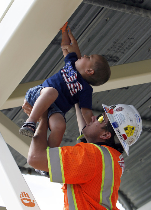 Francisco Kjolseth  |  The Salt Lake Tribune
Chris Dillman holds his son Marshall, 3, as he places a high mark on a bridge. The Dillmans were among participants in a community event Thursday to decorate the pedestrian bridge that is planned for placement at 8200 S. and U-111. The bridge has sat in open storage for several months after being removed from Bangerter Highway.