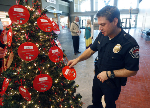 Francisco Kjolseth  |  The Salt Lake Tribune
West Valley City Police officer Devin Novara picks a name from the West Valley City Giving Tree at Valley Fair Mall on Tuesday, Nov. 27, 2012, benefiting 176 youth from 58 families. Those interested in supporting the program can choose and check out a name from the trees located near the Valley Fair Mall Customer Service Center; service representatives will provide a list of the child's needs and holiday wishes. Shoppers are then asked to return the unwrapped gifts to the desk before Dec. 15. The West Valley City Police Department's Community Services Section started the tradition several years ago when a family they were working with experienced multiple tragedies and were left with no resources for the holidays. The department now coordinates with a local organization that works with low-income families in the city to choose names for the tree.