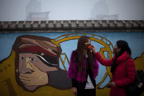 A woman helps adjust a mask for her friend outside an amusement park on a hazy day in Beijing Saturday, Jan. 12, 2013. Air pollution levels in China's notoriously dirty capital were at dangerous levels Saturday, with cloudy skies blocking out visibility and warnings issued for people to remain indoors. (AP Photo/Alexander F. Yuan)