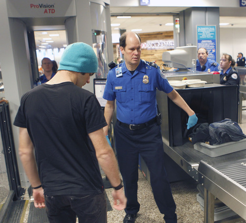 Al Hartmann  |  The Salt Lake Tribune
TSA agent helps flier's get personal carry ons onto conveyor belt for X-ray scanning before sending him through the imaging booth, left, at Salt Lake City International Airport, Terminal 2, security checkpoint Tuesday January 15 at 7:30 a.m.  The booth uses radio frequency technology that detects concealed objects made of any material. For privacy it does not create a life-like image.   Scan data is processed by software without human intervention to determine if any threats are present. Potential threat areas are then presented to the operator using a generic mannequin that resembles a human outline.