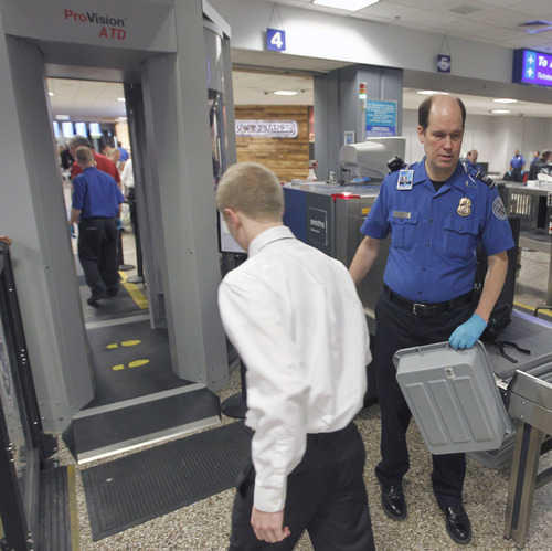 Al Hartmann  |  The Salt Lake Tribune
TSA agent helps flier's get personal carry ons onto conveyor belt for X-ray scanning before sending him through the imaging booth, left, at Salt Lake City International Airport, Terminal 2, security checkpoint Tuesday January 15 at 7:30 a.m.  The booth uses radio frequency tecnology that detects concealed objects made of any material. For privacy it does not create a life-like image.   Scan data is processed by software without human intervention to determine if any threats are present. Potential threat areas are then presented to the operator using a generic mannequin that resembles a human outline.