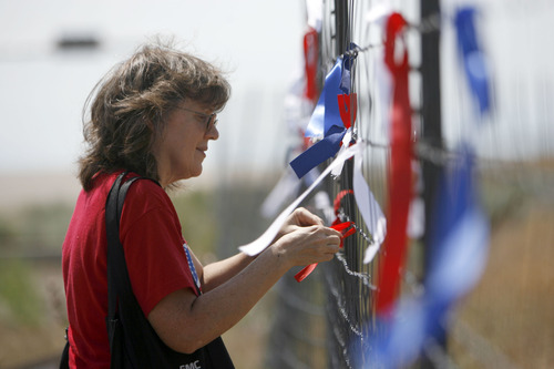 Francisco Kjolseth  |  The Salt Lake Tribune
Susan Barretta of Salt Lake ties a ribbon on the outer most perimeter fence of the new NSA Data Center along Redwood road across from Camp Williams as he joins other opponents of the new facility on the 4th of July.