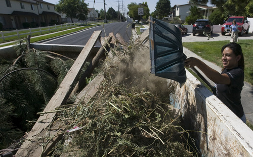 Rick Egan  |  The Salt Lake Tribune
Kotty Alvarez shovels yard waste into the garbage bin in front of her house in Taylorsville on Friday. Taylorsville placed large garbage bins in each neighborhood for a day as part of the annual cleanup program.