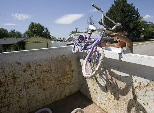 Rick Egan  | The Salt Lake Tribune 

Dakoda Aguirre tosses a bicycle into the garbage bin in front of his house in Taylorsville, Friday, July 26, 2013. Taylorsville placed large garbage bins in each neighborhood for a day as part of the annual cleanup program.