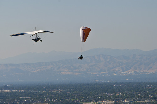 Chris Detrick  |  The Salt Lake Tribune
With pollution visible in the background, a paraglider and hang glider fly over Point of the Mountain Flight Park at Steep Mountain near Geneva Rock Products in Draper Friday July 19, 2013. ]