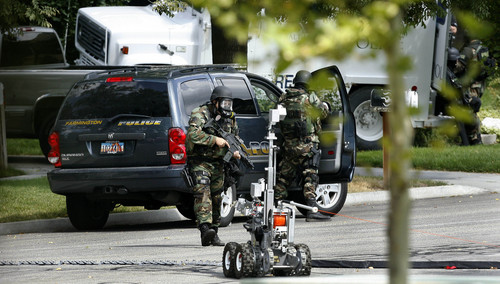 Farmington - Police officers take cover behind a Farmington Police vehicle as a remote control robot advances towards a truck that Brian Wood holed up in outside his home in Farmington following a reported fight with his wife earlier in the day Sept. 22, 2008. The robot was driven next to the truck and released tear gas towards the vehicle. Steve Griffin/The Salt Lake Tribune 9/22/08