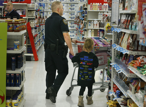 Scott Sommerdorf   |  The Salt Lake Tribune
Sarah Kuddes holds Draper officer Josh Harris' hand as they look for things for her during the "Shop With a Cop" event at the K-Mart in West Jordan, Saturday December 13 2013.