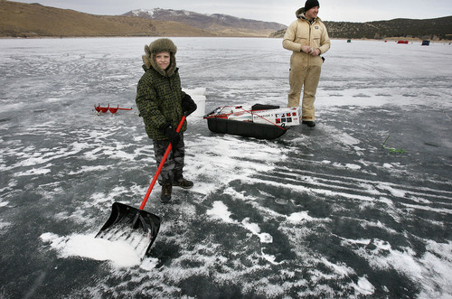 Scott Sommerdorf  |  The Salt Lake Tribune             
Gatlin Bueter, 8, spent some time shoveling snow away from the area he and his father, Tyler, had chosen on the ice at Rockport Reservoir. They were two of the people ice fishing on Rockport Reservoir looking to hook one of more than 30 tagged trout swimming beneath the reservoir's ice Sunday. Lucky anglers who catch one and take it to the Rafter B store can claim prizes ranging from cash to gear.