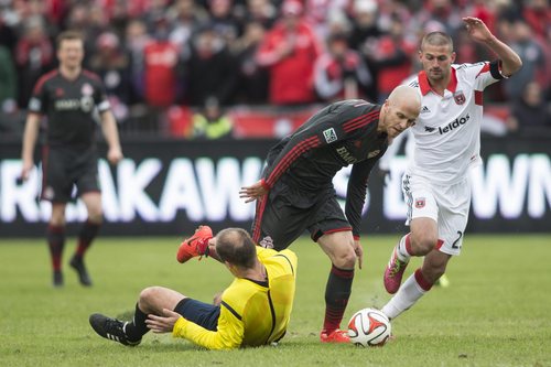 Toronto FC 's Michael Bradley, center, knocks down referee Silviu Petrescu as D.C. United's Perry Kitchen, right, chases during the first half of an MLS soccer game in Toronto on Saturday, March 22, 2014. (AP Photo/The Canadian Press, Chris Young)