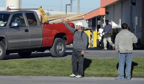 Al Hartmann  |  The Salt Lake Tribune
Day laborers signal two for work to nearby contractor truck waiting outside Home Depot at 2100 South and 300 West on the sidewalk.  Sometimes there are confrontations between security guards and laborers who at times almost ring the parking lot.  Customers who park too close to laborers may find themselves swarmed.  Contractors can negotiate with the waiting men and fill trucks with workers in under 10 seconds.