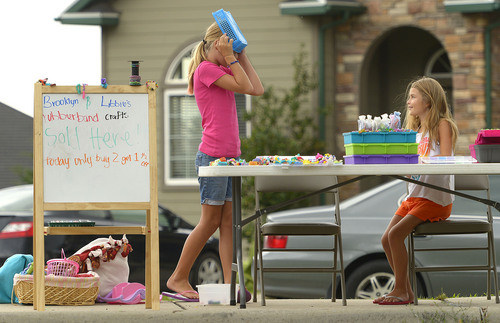 Leah Hogsten  |  The Salt Lake Tribune
The rain has been bothering us," said Libbie Miles, jokingly covering her head from the rain with a basket. "It ruins business." Sisters Libbie Miles, 13, (left) and Brooklyn Miles, 7, set up shop outside their home to sell "sillyband" crafts the two had made, July 29, 2014.