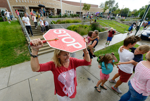 Francisco Kjolseth  |  The Salt Lake Tribune
Julie Pereira, who works the front desk at Bonneville Elementary in Salt Lake shields herself from the rain as she plays double duty as a crossing guard following the first day of school. The school had just been informed that their crossing guards had resigned.