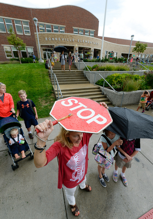 Francisco Kjolseth  |  The Salt Lake Tribune
Julie Pereira, who works the front desk at Bonneville Elementary in Salt Lake shields herself from the rain as she plays double duty as a crossing guard following the first day of school. The school had just been informed that their crossing guards had resigned.