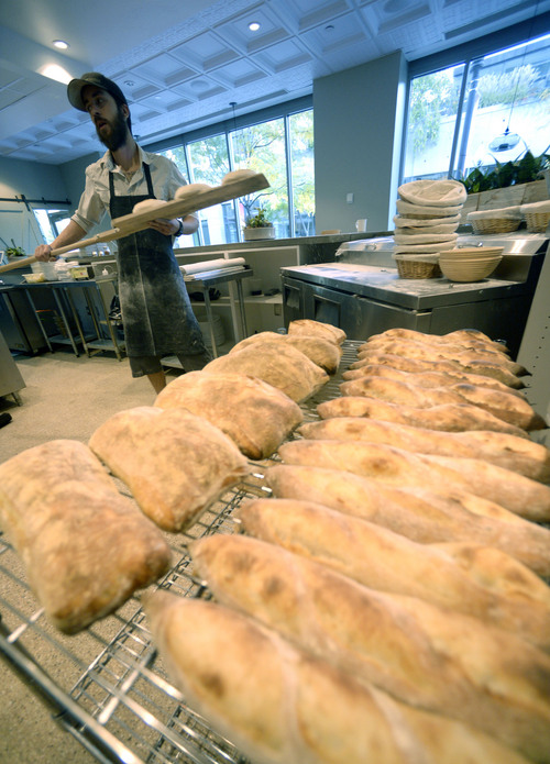 Al Hartmann  |  The Salt Lake Tribune
Ryan Moore, bread baker at From Scratch, loads dough for ciabata bread into the wood-fired pizza oven.  Freshly made baguettes and ciabata cool on a rack.  They are used in the restaurant and extras are sold. The restaurant is the only one in the Salt Lake Valley that grinds its own wheat on-site and sells bread baked from the hearth oven. Moore is one of 15 bakers selected to try out for a spot on the Team USA culinary team.