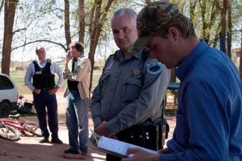 Patrick Pipkin reviews a police report concerning the FLDS's attempted eviction of Pipkin from his home, before filing it with Officer Helaman Barlow of the Colorado City Police Department while Daniel Chatwin talks to Officer Preston Barlow in the background.