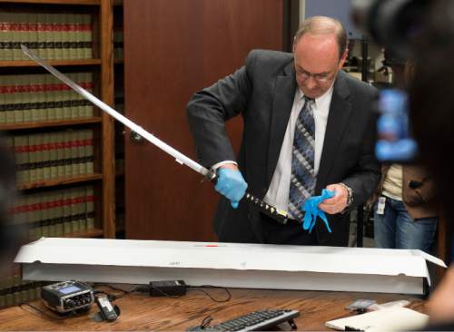 Steve Griffin  |  The Salt Lake Tribune

Utah County Attorney Bureau of Investigations Bureau Chief Jeff Robinson removes the sword carried by Darrien Hunt as Utah County Attorney Jeffrey Buhman addresses the media as he explains the Utah County Attorney's Office's ruling in the officer-involved shooting of Hunt during a press conference in Provo, Monday, November 3, 2014.