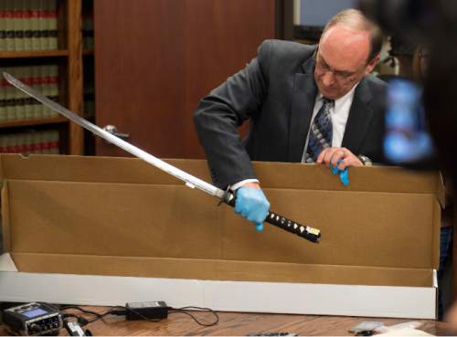 Steve Griffin  |  The Salt Lake Tribune

Utah County Attorney Bureau of Investigations Bureau Chief Jeff Robinson removes the sword carried by Darrien Hunt as Utah County Attorney Jeffrey Buhman addresses the media as he explains the Utah County Attorney Office's ruling in the officer-involved shooting of Hunt during a press conference in Provo, Monday, November 3, 2014.