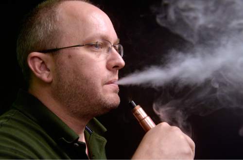 Al Hartmann  |  The Salt Lake Tribune
Aaron Frazier, executive director of Utah Smoke-Free Association, exhales aerosol from a second generation e-cigarette. A battery in the device vaporizes the liquid and gives a similar feel to smoking tobacco cigarettes.The devices continue to gain in popularity as the state of Utah and local health departments clamp down, trying to keep them away from children and teenagers and ensure the labels show the true content of nicotine.
The governor wants to tax e-cigarettes, and Utah lawmakers are likely to take up legislation again.