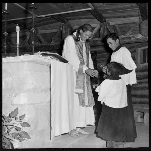 Salt Lake Tribune archive

Father Liebler holding church services at St. Cristopher's Mission in Bluff, Utah in 1950. St. Christopher's Episcopal Mission was established in 1943 when H. Baxter Liebler, an Episcopal priest from Old Greenwich, Connecticut came to Bluff to establish a mission among the Navajo people. St Christopher's is named after the patron saint of travelers.  When Father Liebler arrived in Bluff, there were no missions, schools, or medical/hospital facilities for the Navajo living in this remote Utah section of the reservation. Before arriving in southeast Utah, Father  Liebler studied the Navajo language to make his message comprehensible to the Dineh and compatible with their understanding of harmony.  He participated in Navajo ceremonies, wore his hair in the traditional Navajo style-long, pulled back and wrapped.
A year after the mission was established, a school was started which became the only school for the 1,500 Navajo living in the central part of the Utah strip of the Navajo Reservation. A hospital/ clinic building was completed in 1956.  An estimated 500 babies were born in the clinic during the years it was in operation.