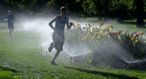 Al Hartmann  |  Tribune file photo 
Runners take advantage of sprinklers to cool down on their training run in Sugar House Park.