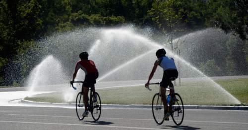 Al Hartmann  |  Tribune file photo
Bicylists take a spin around Sugar House Park as sprinklers water the grass.