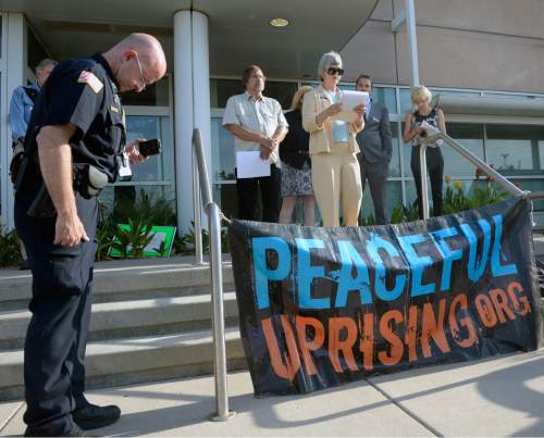 Al Hartmann |  The Salt Lake Tribune
A small group from Peaceful Uprising, Utah Tar Sands Resistance and concerned citizens read statements and performed a skit with children on the steps of the Utah Department of Natural Resources as a security guard records them before a crucial hearing Tuesday, June 30 at the Utah Division of Oil, Gas and Mining in Salt Lake City.
