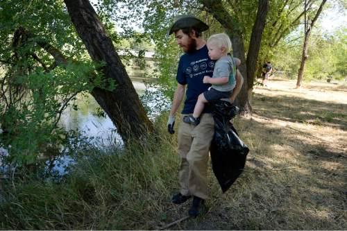 Scott Sommerdorf   |  The Salt Lake Tribune
Paul Inkenbrandt carries his son Fox as he helps during the cleanup of the Jordan River. United by Blue hosted a cleanup of the Jordan River in advance of the Outdoor Retailers summer market. The organization pledges to remove one pound of trash from oceans and waterways for every product sold. Volunteers collected 531 pounds of trash.