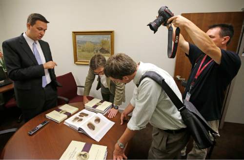 People look at pictures of the smooth, brown, egg-sized rock shown in the printer's manuscript of the Book of Mormon following a news conference Tuesday, Aug. 4, 2015, at The Church of Jesus Christ of Latter-day Saints Church History Library, in Salt Lake City. The Mormon church for the first time is publishing photos of a small sacred stone it believes founder Joseph Smith used to help translate the story that became the basis of the religion. The Mormon church is taking another step in its push to be more transparent, and is releasing more historical documents that shed light on how Joseph Smith formed the religion. (AP Photo/Rick Bowmer)