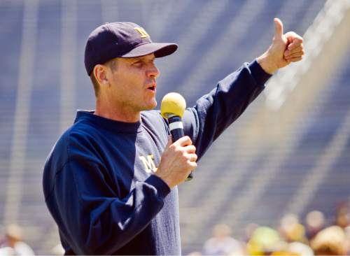 FILE - In this Aug. 6, 2015, file photo, Michigan head coach Jim Harbaugh greets fans in Michigan Stadium during the NCAA college football team's annual media day in Ann Arbor, Mich. It felt at times like Jim Harbaugh's every move was being monitored this offseason, such is the level of excitement and anticipation surrounding his arrival at Michigan. (AP Photo/Tony Ding, File)