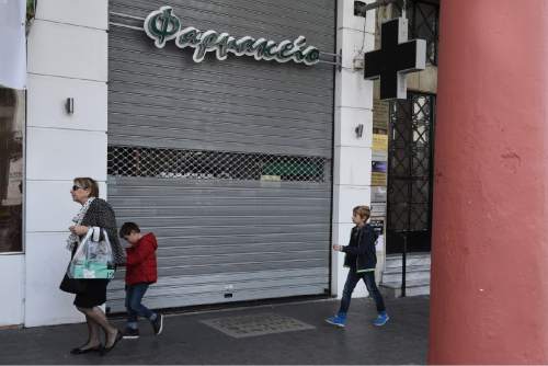 People walk past a shuttered pharmacy during the first day of a strike by the pharmacy owners association in the northern Greek city of Thessaloniki, Monday, Oct. 26, 2015. Pharmacists are on strike to protest against new reforms in their sector. A leading European Union official said Monday that Greece's bailout talks with its international creditors are broadly on track, but the country still has much work to do, in little time. (AP Photo/Giannis Papanikos)