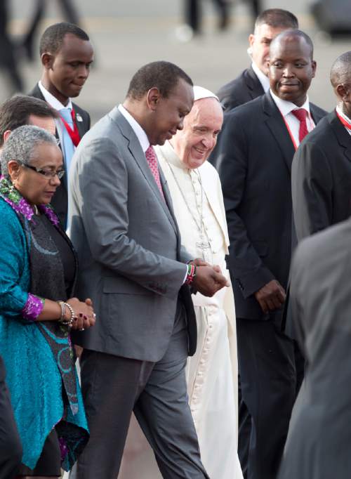 Pope Francis, center, walks with Kenya's President Uhuru Kenyatta, center-left, and Kenya's First Lady Margaret Kenyatta, left, on his arrival at the airport in Nairobi, Kenya Wednesday, Nov. 25, 2015. Pope Francis left Wednesday for his first-ever visit to the continent, a whirlwind pilgrimage to Kenya, Uganda and the Central African Republic, bringing a message of peace and reconciliation to an Africa torn by extremist violence. (AP Photo/Ben Curtis)