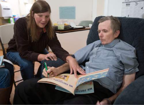 Steve Griffin  |  The Salt Lake Tribune

Utah author and longtime friend Carol Lynch Williams shows Rick Walton, who has written more than 1,000 picture books, a newly published book from one of Rick's former students as she visits him at Orchard Park Rehab in Orem in October 2015. Walton has been diagnosed with a terminal brain tumor and lives in the care facility where author friends ó famous and not ó visit nearly daily, some bringing their latest manuscripts seeking Rick's feedback.