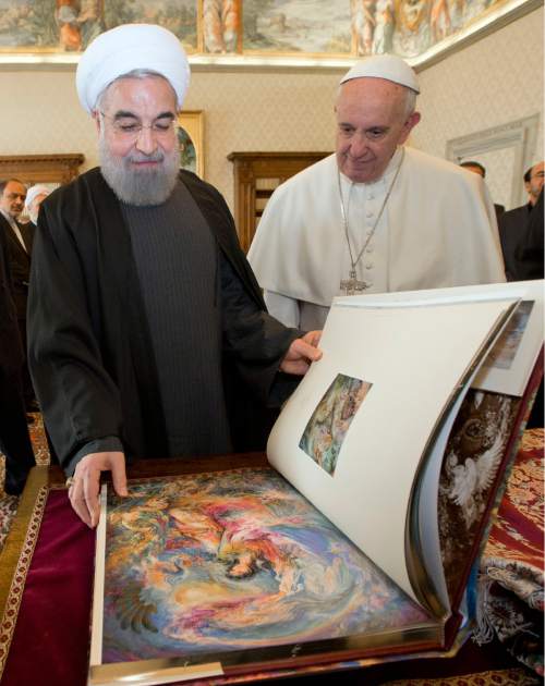 Iranian President Hassan Rouhani, left, leafs through a book he gave to Pope Francis as a gift, during their private audience at the Vatican,Tuesday, Jan. 26, 2016. Iran's president has paid a call on Pope Francis at the Vatican during a European visit aimed at positioning Tehran as a potential top player in efforts to resolve Middle East conflicts, including Syria's civil war. (AP Photo/Andrew Medichini, Pool)