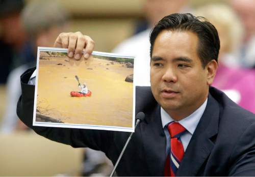 Utah Attorney General Sean Reyes holds a photograph from the massive spill from the abandoned Colorado gold mine that sent toxic wastewater flowing into Utah and at least two other states during the State Water Development Commission meeting Tuesday, Aug. 18,  2015, in Salt Lake City. Reyes told Utah lawmakers that he first wants to see how the Environmental Protection Agency proposes to fix the damage to the state's waters, but legal action will be on the table if their actions fall short. (AP Photo/Rick Bowmer)