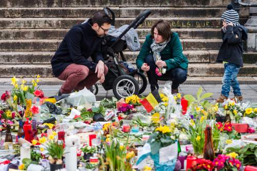 A family lights a candle at floral tributes at a memorial site at the Place de la Bourse in Brussels, Sunday, March 27, 2016. In a sign of the tensions in the Belgian capital and the way security services are stretched across the country, Belgium's interior minister appealed to residents not to march Sunday in Brussels in solidarity with the victims. (AP Photo/Geert Vanden Wijngaert)
