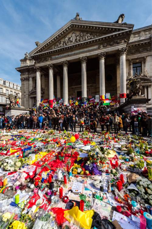 People gather at floral tributes at a memorial site at the Place de la Bourse in Brussels, Saturday, March 26, 2016.  Brussels airport officials say flights won't resume before Tuesday as they assess the damage caused by twin explosions in the terminal earlier this week. (AP Photo/Geert Vanden Wijngaert)