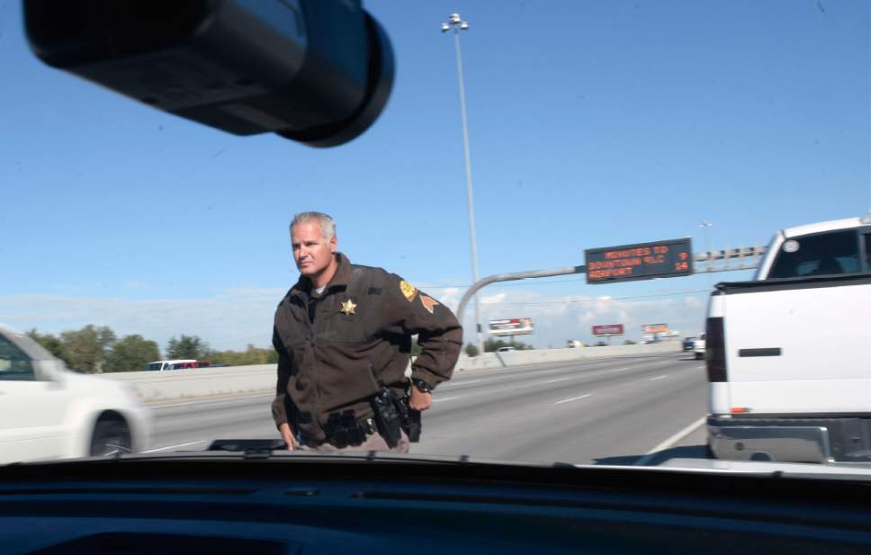 Al Hartmann  |  The Salt Lake Tribune
UHP Sgt. Danny Allen looks for cars illegally using the HOV lanes along I-15 in Salt Lake valley Wednesday Oct. 6. He returns to his patrol car to write a ticket for incorrect use of the HOV lane to the white truck, right. Utah Department of Transportation and Utah Highway Patrol are partnering and launching an enforcement blitz to educate drivers how to correctly use the express lanes.   Utah's Express Lanes are the longest continuous in the country stretching 72 miles from Layton to Spanish Fork.