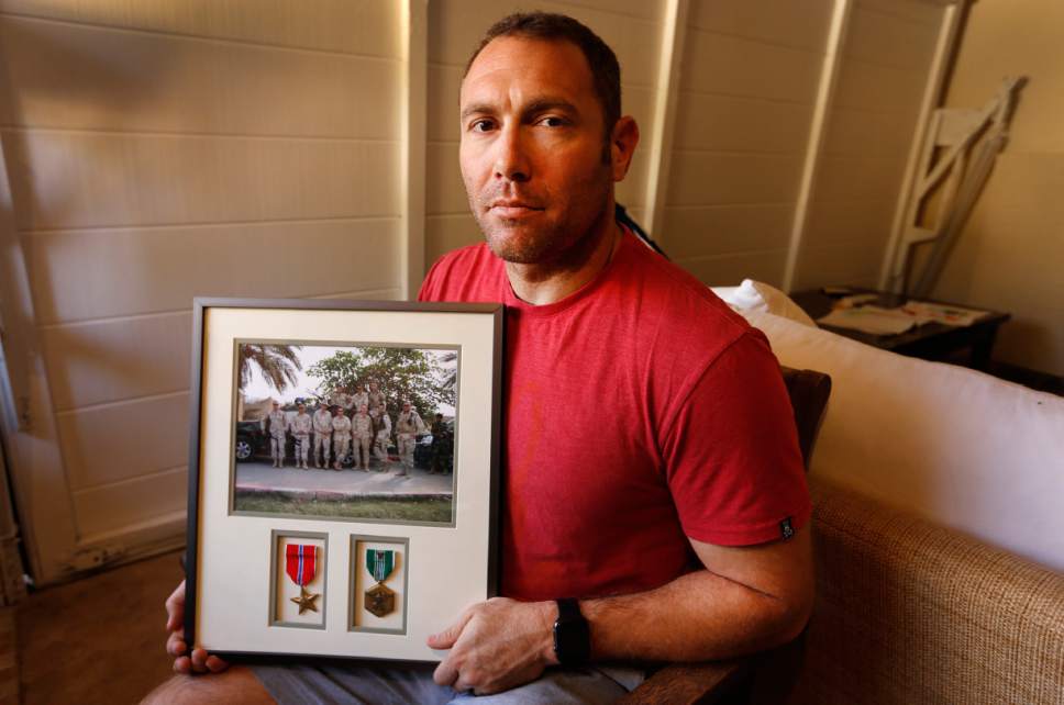 FILE - In this Friday, Oct. 21, 2016 file photo, Robert D'Andrea, a retired Army major and Iraq war veteran, holds a frame with a photo of his team on his first deployment to Iraq in his home in Los Angeles. Nearly 10,000 California National Guard soldiers have been ordered to repay huge enlistment bonuses a decade after signing up to serve in Iraq and Afghanistan, the Los Angeles Times reported Saturday. (Al Seib/Los Angeles Times via AP, File)