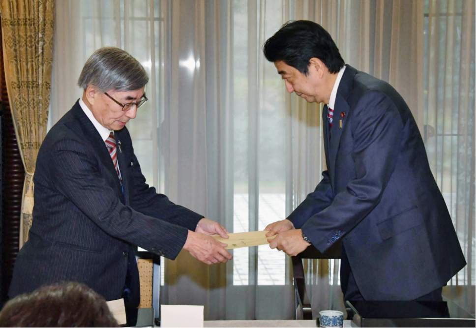 Japanese Prime Minister Shinzo Abe, right, receives a letter addressed to Russian President Vladimir Putin from Kimio Waki, head of a group of former residents of the Russian-held islands off Japan's major northern island of Hokkaido, during their meeting at the prime minister's official residence in Tokyo Monday, Dec. 12, 2016. Japan's Trade Minister Hiroshige Seko said later Monday his country's economic relations with Russia have grown more smoothly than political ties, with about 30 joint projects ready to be signed regardless of a breakthrough in territorial issues. Seko said that a final decision on the projects is up to Abe, who is to meet with Putin in Japan later this week. (Kyodo News via AP)