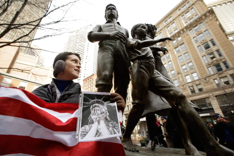 Molly Hitt, of Boston, displays an American flag while standing in front of a memorial to the Irish potato famine, right, during a rally called "We Will Persist," Tuesday, Feb. 21, 2017, in Boston. According to organizers the rally was held to send a message to Republicans in Congress and the administration of President Donald Trump that they will continue to press for immigration rights and continued affordable healthcare coverage. (AP Photo/Steven Senne)