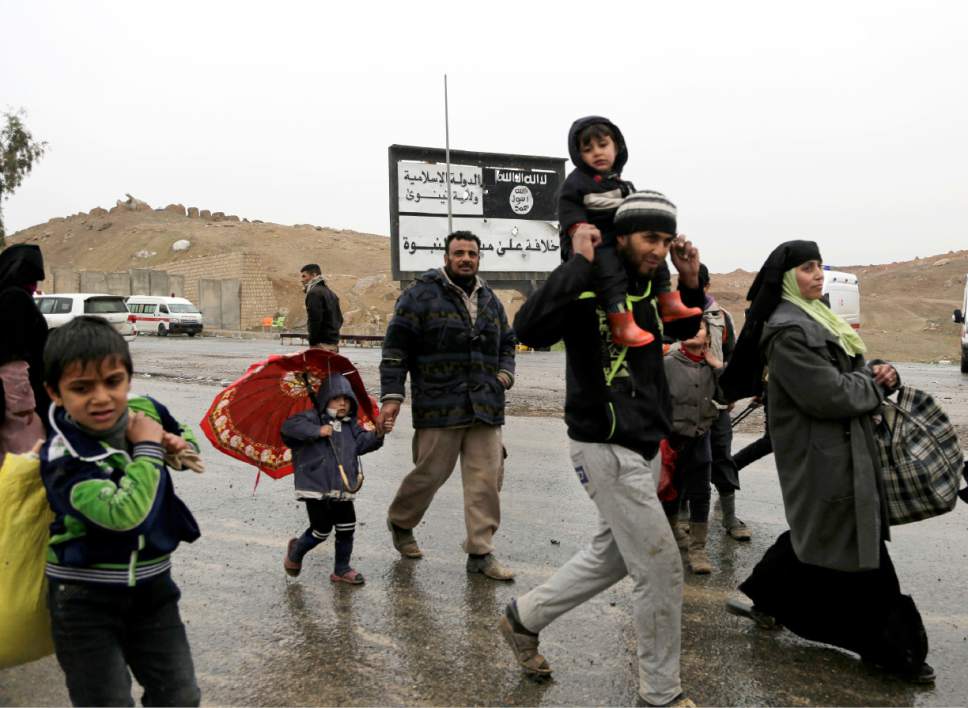 Families walk past an Islamic State sign while fleeing clashes between Iraqi forces and Islamic State group militants in western Mosul, Thursday, March 2, 2017. The United Nations says over 28,000 people have fled the city since the operation to retake its remaining militant-held western districts was launched last month. (AP Photo/Susannah George)